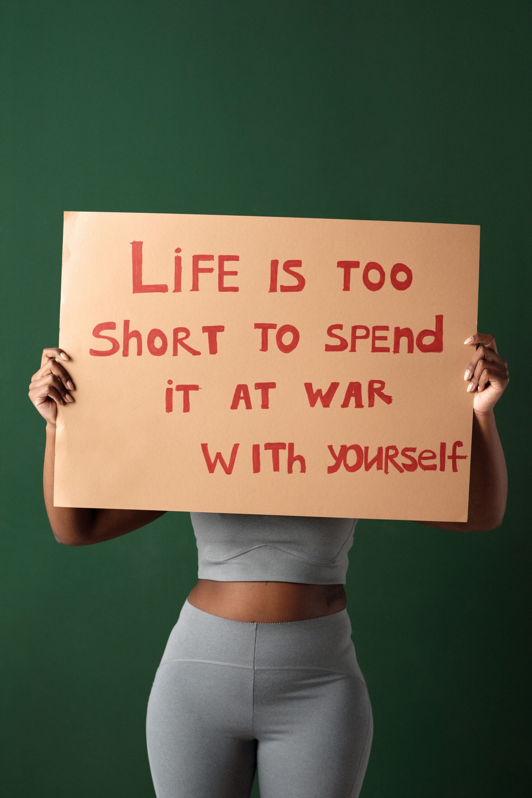 Woman holding motivational sign about self-love and peace on green background.